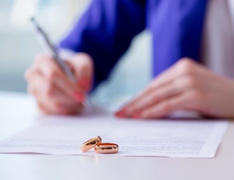 A person writing on paper with two rings sitting next to it.