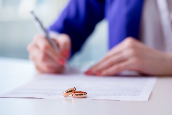A person writing on paper with two rings sitting next to it.