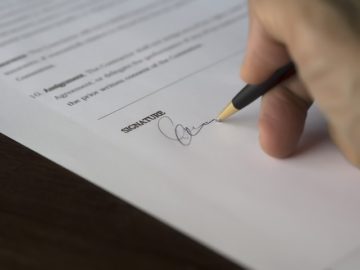A person signing a document with a pen.